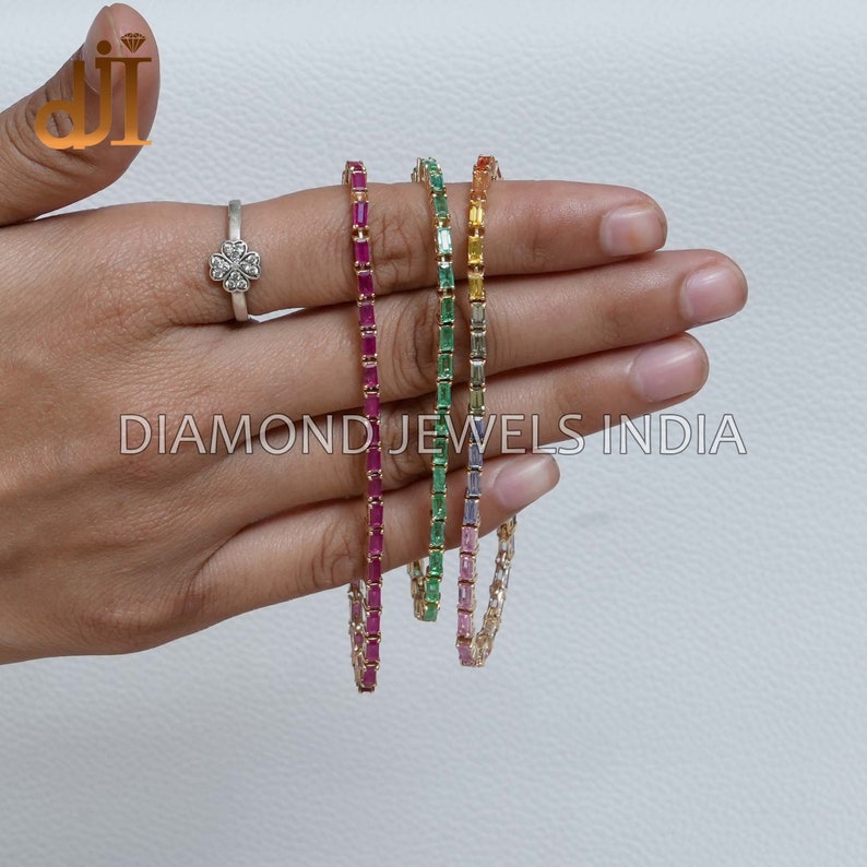 May include: Four gold bracelets with different colored gemstones. The bracelets are made of small, square-shaped gemstones set in a continuous line. The colors of the gemstones are red, green, yellow, and purple.