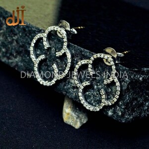 May include: A pair of silver earrings with a flower design set with small diamonds. The earrings are on a dark grey background.