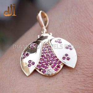 May include: Gold-toned ladybug pendant with ruby-colored and white gemstones. The pendant features a detailed design with a loop for a chain. The ladybug's body is filled with red stones, and the wings have a smooth, polished finish.