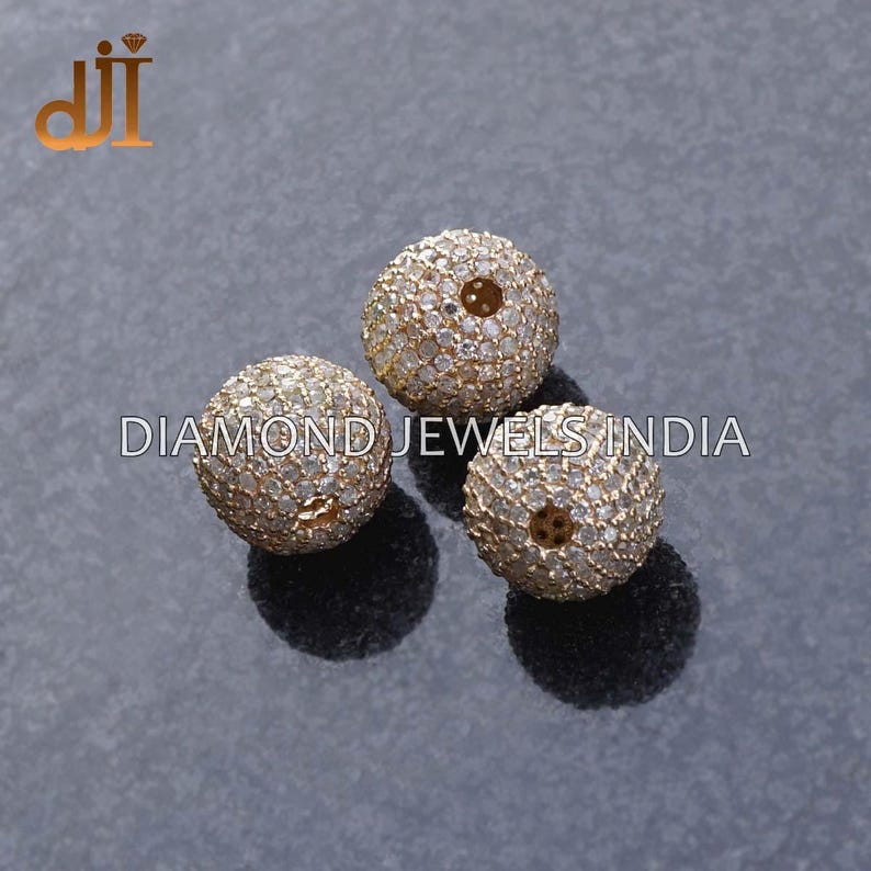 K&ouml;nnte beinhalten: Drei runde, goldfarbene Perlen, besetzt mit kleinen, klaren Steinen. Jede Perle hat ein zentrales Loch und liegt vor einem dunkelgrauen Hintergrund. Der Text "DIAMOND JEWELS INDIA" ist sichtbar.