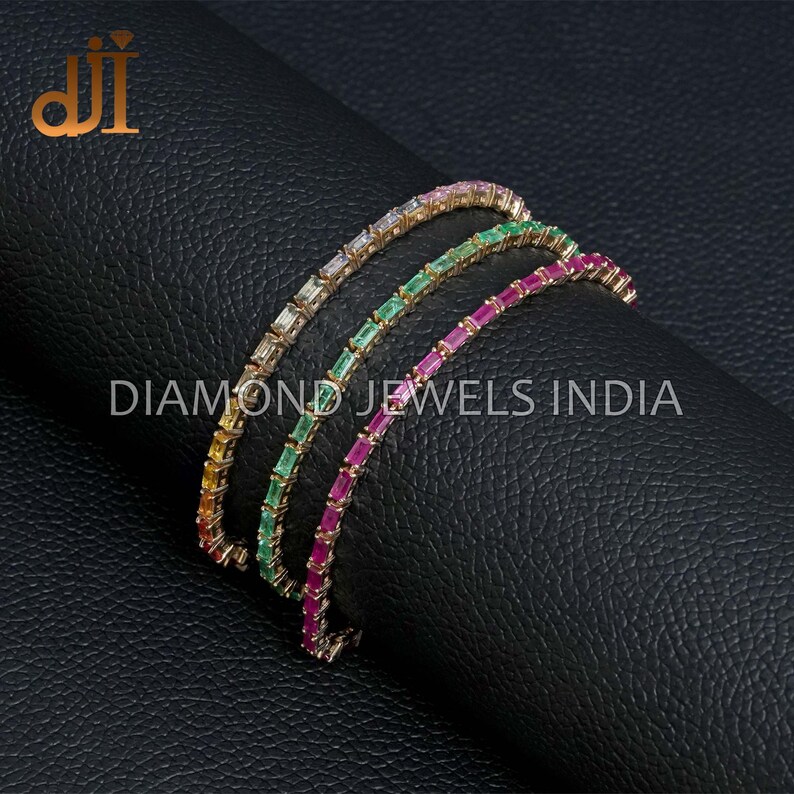 May include: Three gold tennis bracelets with different colored gemstones. The bracelets feature a row of emerald-cut gemstones in pink, green, and yellow.