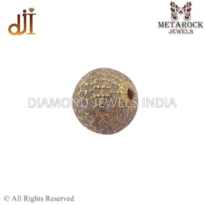 K&ouml;nnte beinhalten: Eine goldfarbene, kugelf&ouml;rmige Perle, besetzt mit kleinen, klaren Edelsteinen. Die Perle hat eine strukturierte Oberfl&auml;che und ein kleines Loch. Die Worte "DIAMOND JEWELS INDIA" sind im Hintergrund aufgedruckt.