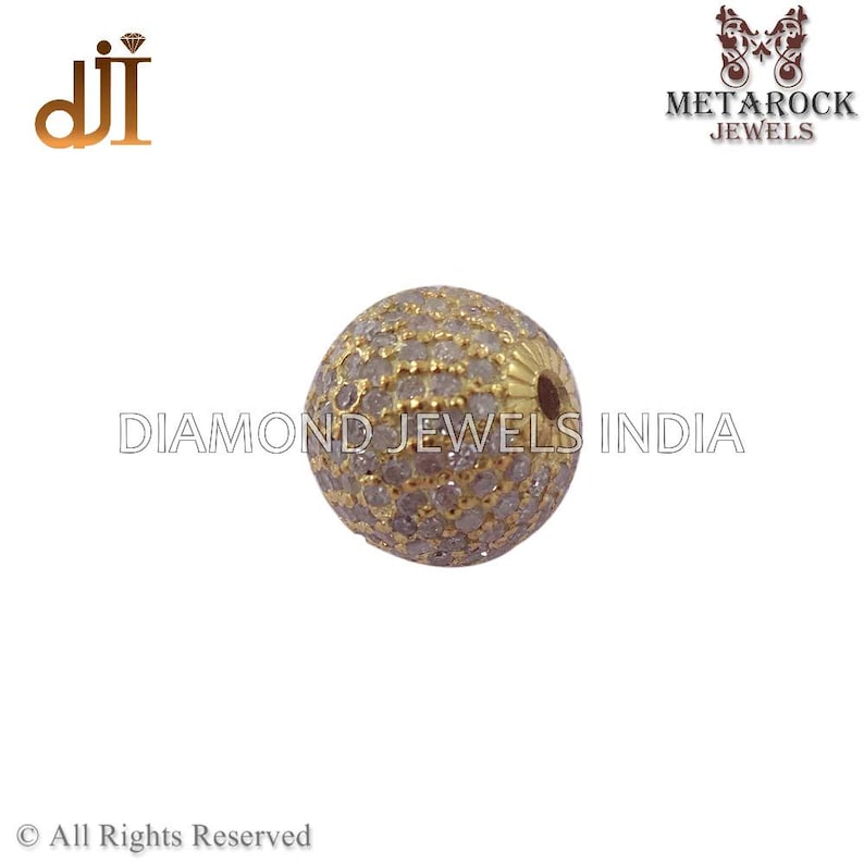 K&ouml;nnte beinhalten: Eine goldfarbene, kugelf&ouml;rmige Perle, besetzt mit kleinen, klaren Edelsteinen. Die Perle hat eine strukturierte Oberfl&auml;che und ein kleines Loch. Die Worte "DIAMOND JEWELS INDIA" sind im Hintergrund aufgedruckt.