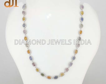 May include: A multi-colored gemstone necklace with oval-shaped stones in various colors, including yellow, blue, and purple. The necklace is set in a silver metal and is displayed on a white mannequin. The text "DIAMOND JEWELS INDIA" is visible.