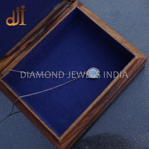 May include: A silver chain necklace with a round pendant featuring a grey stone surrounded by a halo of small diamonds. The necklace is in a wooden box with a blue velvet lining. The text "DIAMOND JEWELS INDIA" is visible on the box.