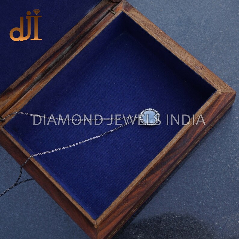 May include: A silver chain necklace with a round pendant featuring a grey stone surrounded by a halo of small diamonds. The necklace is in a wooden box with a blue velvet lining. The text "DIAMOND JEWELS INDIA" is visible on the box.