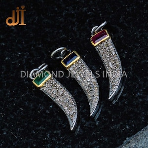 May include: Three silver pendants shaped like a curved horn, each with a different coloured gemstone at the top. The gemstones are red, blue, and green. The pendants are covered in small white stones.