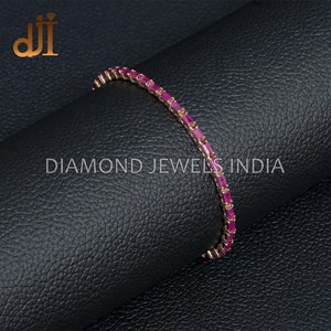May include: A gold bracelet with a row of pink rectangular gemstones. The bracelet is on a black textured surface. DIAMOND JEWELS INDIA is printed on the surface.