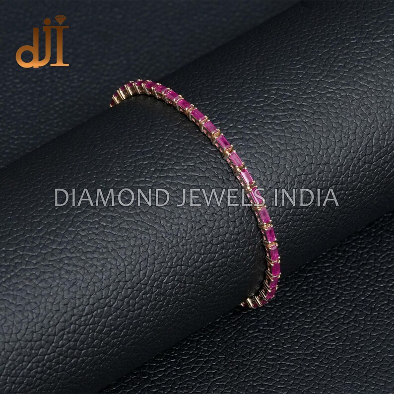 May include: A gold bracelet with a row of pink rectangular gemstones. The bracelet is on a black textured surface. DIAMOND JEWELS INDIA is printed on the surface.