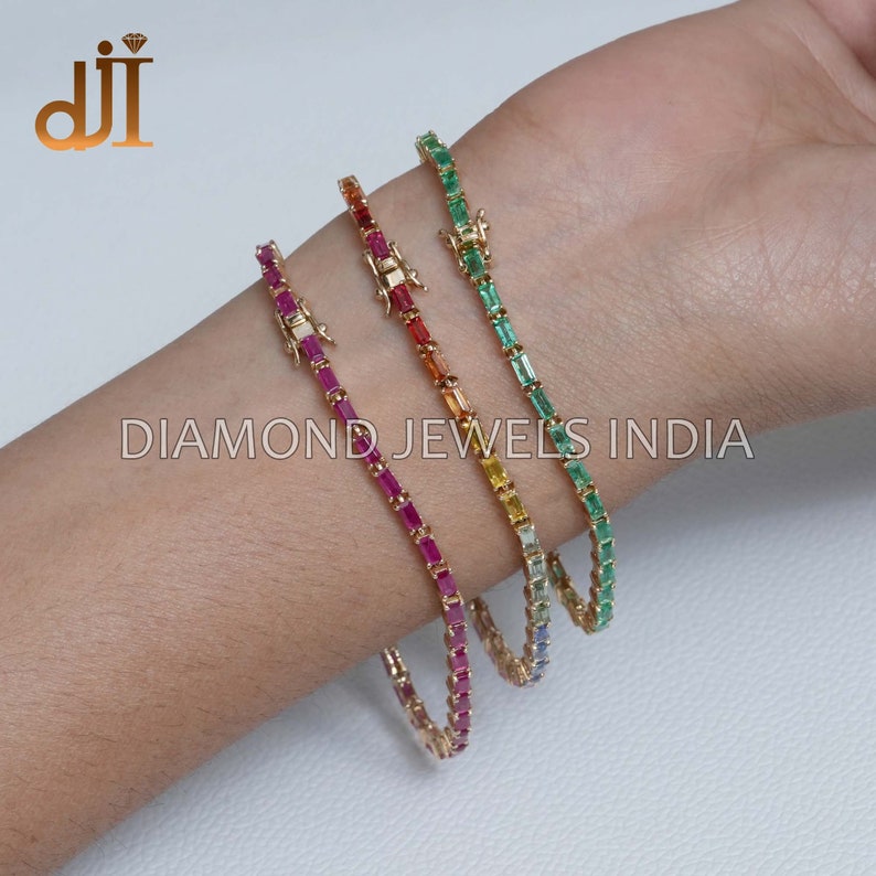 May include: Four gold bracelets with different colored gemstones. The bracelets are made of small, square-shaped gemstones set in a gold chain. The gemstones are red, orange, yellow, and green.