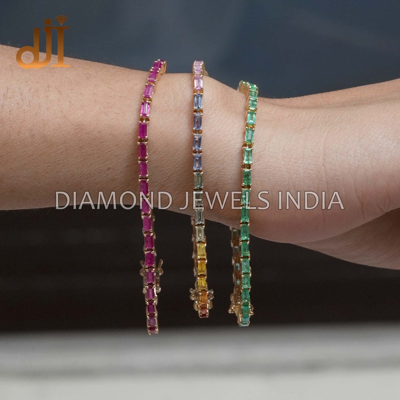 May include: Four gold bracelets with different colored gemstones. The bracelets are made of small, rectangular gemstones set in a gold chain. The gemstones are red, blue, yellow, and green.