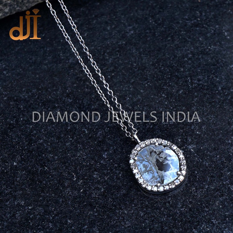 May include: A silver chain necklace with a large, oval-shaped pendant. The pendant features a clear, faceted gemstone surrounded by a halo of smaller, sparkling gemstones.