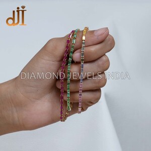 May include: Three gold bracelets with different colored gemstones. The bracelets are made of small, rectangular-shaped gemstones. The colors of the gemstones are pink, green, and yellow.