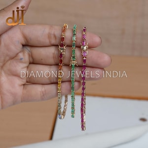 May include: Four gold bracelets with different colored gemstones. The bracelets are made with a row of rectangular gemstones. The gemstones are red, green, yellow, and blue.