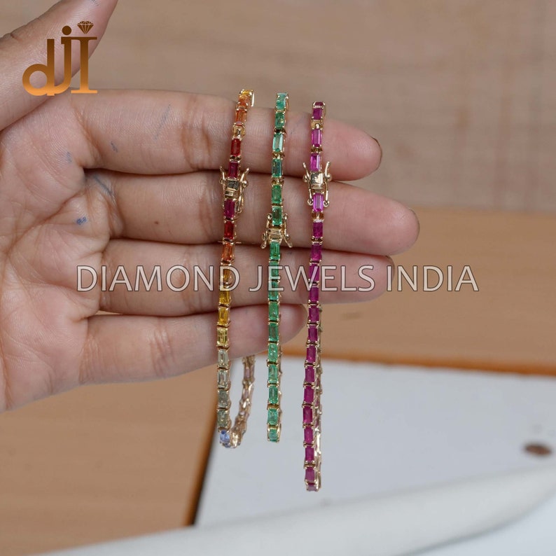 May include: Four gold bracelets with different colored gemstones. The bracelets are made with a row of rectangular gemstones. The gemstones are red, green, yellow, and blue.
