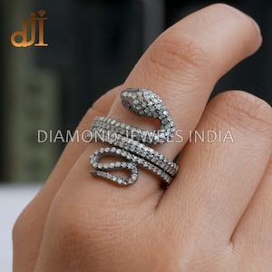 May include: A silver snake ring with a black diamond encrusted body and a pink stone for an eye. The ring is wrapped around a finger.