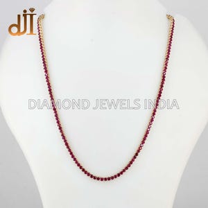 Könnte beinhalten: Eine zarte goldene Halskette, verziert mit zahlreichen kleinen, leuchtend roten Edelsteinen. Die Halskette wird auf einer weißen Schaufensterpuppe präsentiert, die ihr elegantes Design zeigt. Der Text "DIAMOND JEWELS INDIA" ist sichtbar.