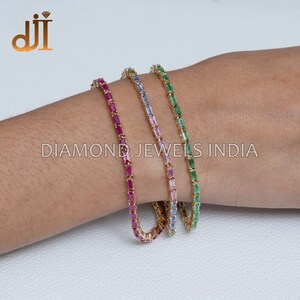 May include: Three gold bracelets with different colored gemstones. The bracelets are made of small, rectangular gemstones set in gold. The gemstones are red, blue, and green.