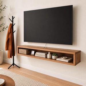 May include: A rectangular, wall-mounted wooden floating shelf positioned beneath a large, black flat-screen television. The shelf features an open storage compartment containing a woven basket, books, a small vase, a succulent, and a bowl.