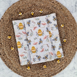 May include: White fabric with a repeating pattern of honeycombs, bees, and flowers. The fabric is decorated with small yellow and black bee charms.