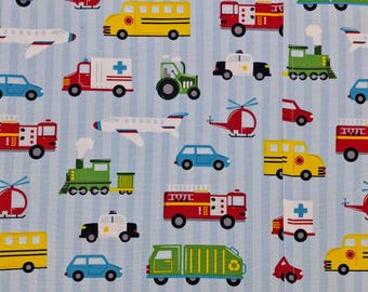 May include: A light blue fabric with a repeating pattern of various vehicles, including school buses, fire trucks, ambulances, airplanes, helicopters, trains, police cars, and cars. The vehicles are in bright colors.