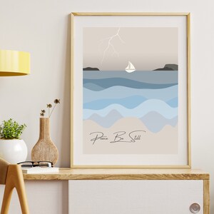 Pode incluir: Impressão de arte emoldurada com uma paisagem marinha minimalista com um veleiro, ondas e um raio. A paleta de cores inclui tons de azul, bege e cinza. As palavras "Peace Be Still" estão escritas em itálico na parte inferior.