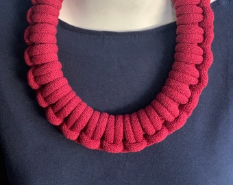Op de afbeelding: Een rode gecrochete ketting gemaakt van dik touw. De ketting wordt getoond op een mannequin.