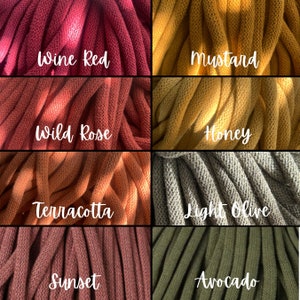 Op de afbeelding: Close-up van acht verschillende gekleurde garenmonsters. Kleuren zijn wijnrood, mosterd, wilde roos, honing, terracotta, licht olijfgroen, zonsondergang en avocado. Elk monster heeft een handgeschreven label met de kleurnaam.