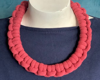 Op de afbeelding: Een dikke, rode, gecrochete ketting gemaakt van touw. De ketting wordt getoond op een mannequin met een donkerblauw shirt.