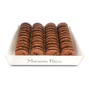 May include: A white box filled with 36 chocolate macarons, each with chocolate sprinkles. The box has the words "Macaron Bites" printed on the front.