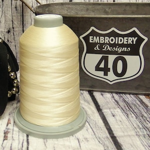 May include: A spool of off-white embroidery thread with a gray plastic base. The spool is labeled "Embroidery & Designs 40".