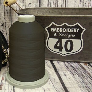 Op de afbeelding: Een spoel donkerbruin borduurgaren met een wit label met de tekst "Embroidery & Designs 40".