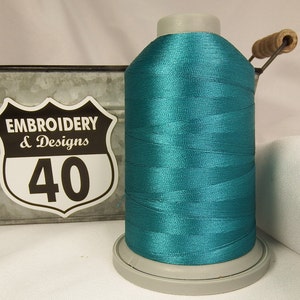 May include: A spool of teal embroidery thread with the label "Embroidery & Designs 40" on a metal container.