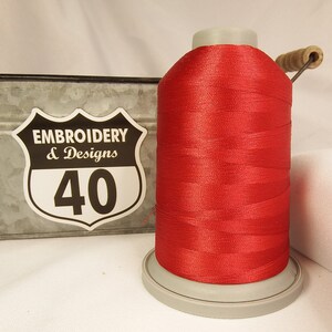Op de afbeelding: Een spoel rood borduurgaren met een wit label waarop "Embroidery & Designs 40" staat.