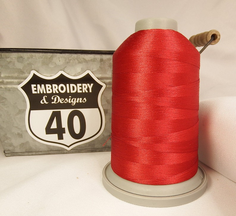 Op de afbeelding: Een spoel rood borduurgaren met een wit label waarop "Embroidery & Designs 40" staat.