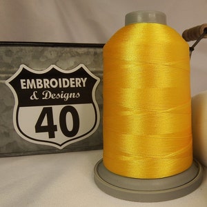 Op de afbeelding: Een spoel met felgele borduurgaren met een label met de tekst "Embroidery & Designs 40".
