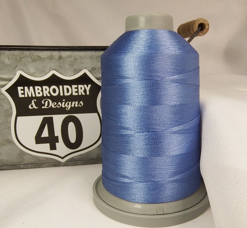 Op de afbeelding: Een spoel lichtblauw borduurgaren met een wit label met de tekst "Embroidery & Designs 40".