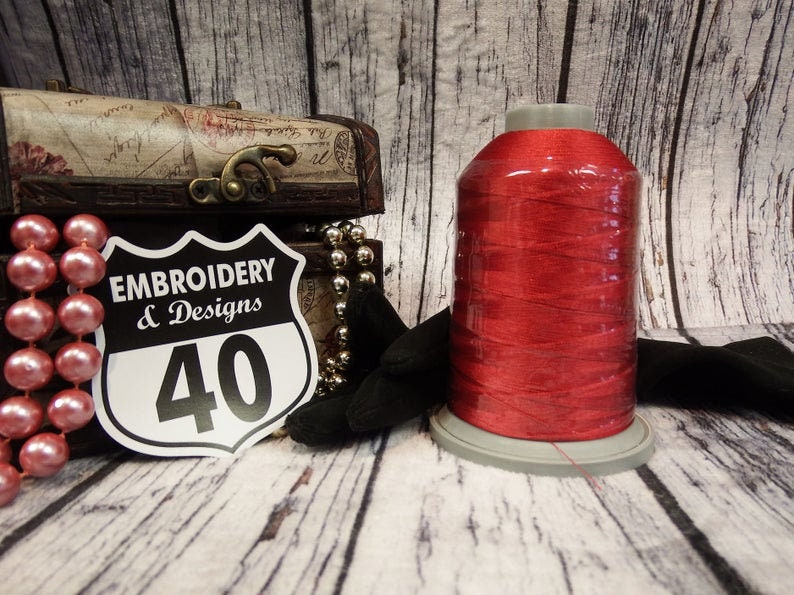 Op de afbeelding: Een spoel rood borduurgaren met een wit label waarop "Embroidery & Designs 40" staat.