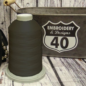 May include: A spool of dark brown embroidery thread on a gray base. The spool is labeled "Embroidery & Designs 40" with a white background and black text.