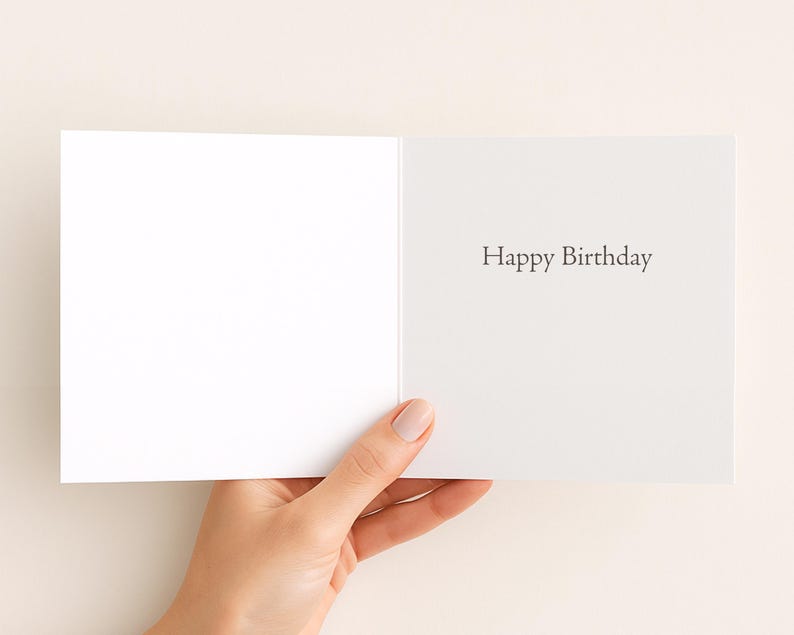 A hand holding an open white greeting card with the text "Happy Birthday" written on it.