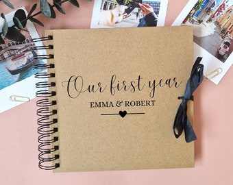 Könnte beinhalten: Ein braunes Fotoalbum mit einem schwarzen Band und dem Text "Our first year Emma & Robert" auf dem Einband.