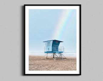 Könnte beinhalten: Gerahmter Druck eines blauen Rettungsturms an einem Sandstrand unter einem Regenbogen. Der Turm trägt die Nummer 1. Der Himmel ist hellblau.