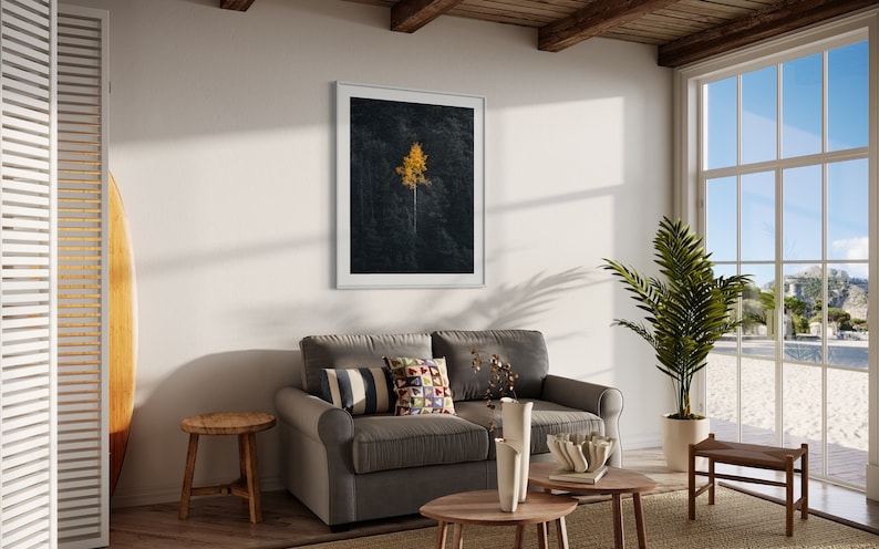 May include: A living room interior with a gray sofa, a wooden coffee table, a potted plant, and a framed print of a single yellow tree against a dark background.
