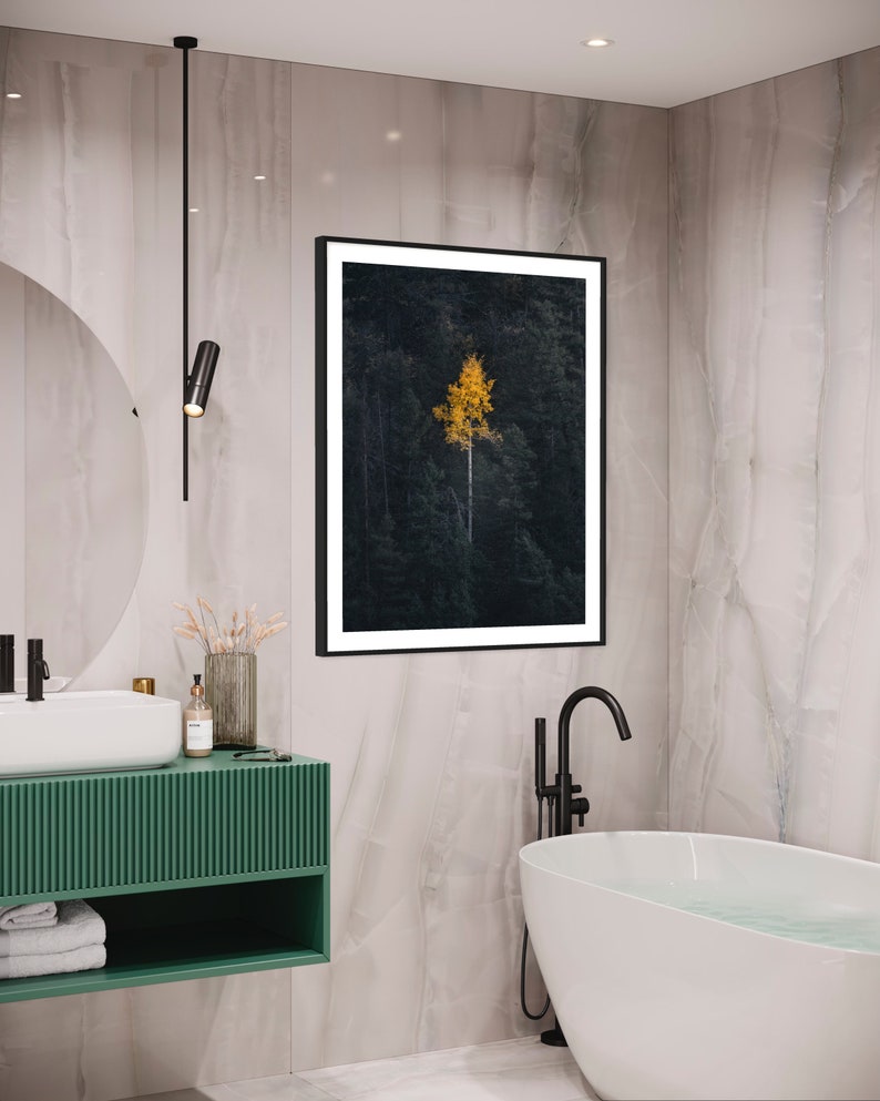 May include: A modern bathroom with a green vanity, a white bathtub, and a black framed picture of a single yellow tree in a dark forest.