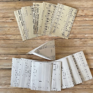 May include: A collection of folded paper items featuring printed musical notes and text. The items are arranged on a wooden surface. Some items are folded into small booklets, while others are folded into a triangular shape. The text includes musical terms and phrases.