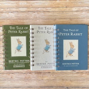 May include: Three spiral-bound notebooks with covers in green, white, and blue. Each features the title "The Tale of Peter Rabbit" and an illustration of a rabbit in a blue jacket. The author's name, Beatrix Potter, and the publisher's name, F. Warne & Co., are also visible.