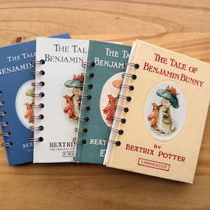 May include: Four spiral-bound notebooks with covers featuring illustrations of Benjamin Bunny from Beatrix Potter's story. The notebooks are in shades of blue, white, and green, with the title "The Tale of Benjamin Bunny" on the cover.