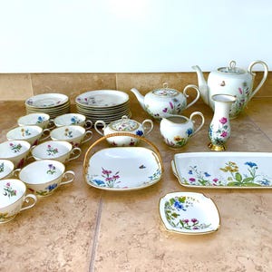 May include: A complete floral tea set with white porcelain cups, saucers, plates, teapots, a creamer, sugar bowl, and serving trays. The set features a delicate floral pattern in pink, blue, and yellow, with gold trim.