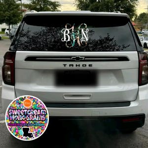 May include: White SUV with a black rear bumper and a black "TAHOE" emblem. The rear window has a floral monogram decal with the letters "B, J, N" in white. A round sticker on the rear bumper says "Sweetcream Monograms Shreveport, Louisiana" with a colorful confetti design.