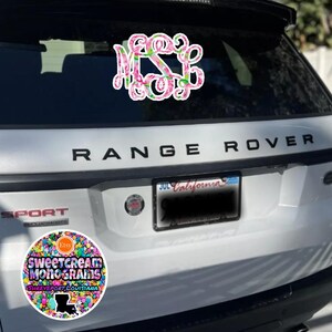 May include: A white Range Rover with a pink and green floral monogram sticker on the back window. The car also has a sticker that says "Sweetcream Monograms Shreveport, Louisiana" with a colorful confetti design and a silhouette of the state of Louisiana.